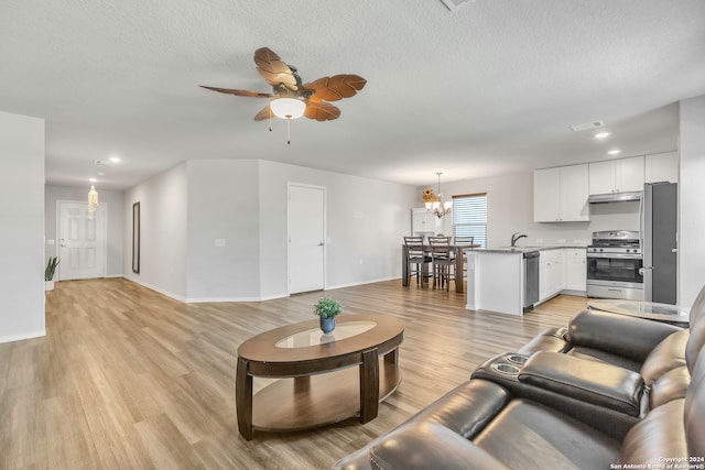 living room with sink, ceiling fan with notable chandelier, light hardwood / wood-style floors, and a textured ceiling