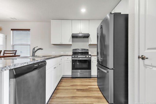 kitchen with stainless steel appliances, white cabinetry, light stone countertops, and light hardwood / wood-style flooring