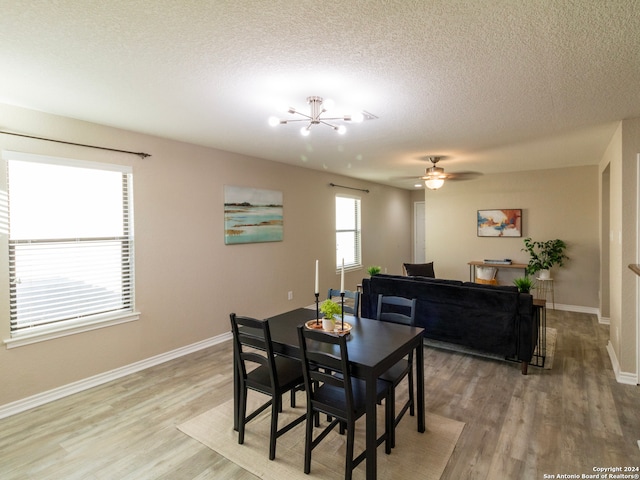 dining space featuring ceiling fan with notable chandelier, wood-type flooring, and a textured ceiling