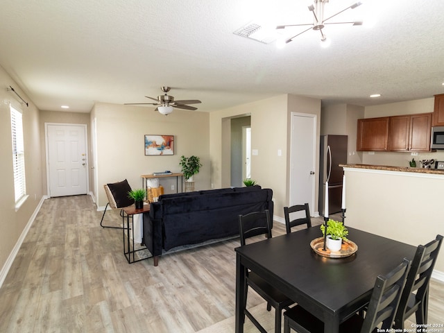 dining area with light hardwood / wood-style flooring, ceiling fan with notable chandelier, and a textured ceiling