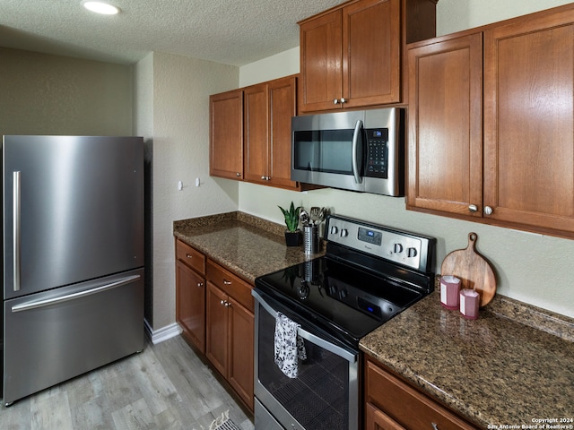 kitchen featuring dark stone countertops, a textured ceiling, appliances with stainless steel finishes, and light hardwood / wood-style flooring