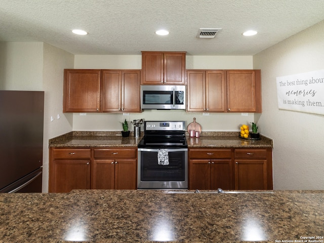 kitchen with a textured ceiling, stainless steel appliances, and dark stone counters