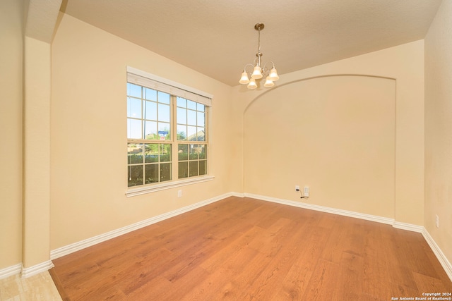 empty room featuring a chandelier, a textured ceiling, and light wood-type flooring