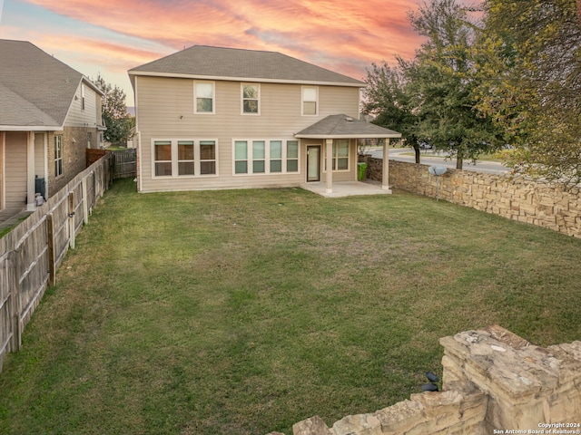 back house at dusk with a patio area and a lawn