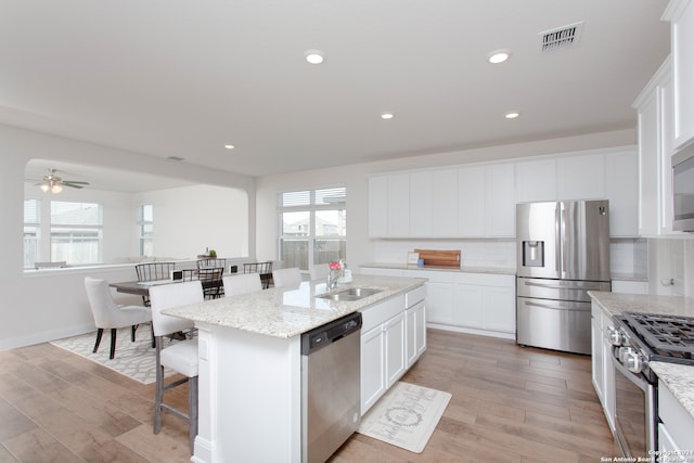 kitchen with sink, stainless steel appliances, tasteful backsplash, an island with sink, and light wood-type flooring