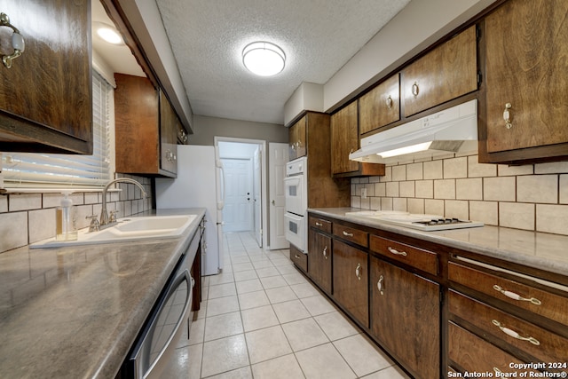 kitchen with white appliances, backsplash, sink, a textured ceiling, and light tile patterned flooring