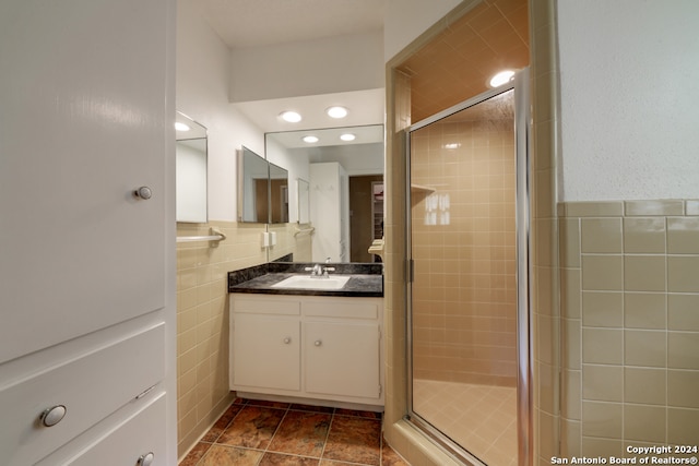 bathroom with a shower with door, vanity, and tile walls