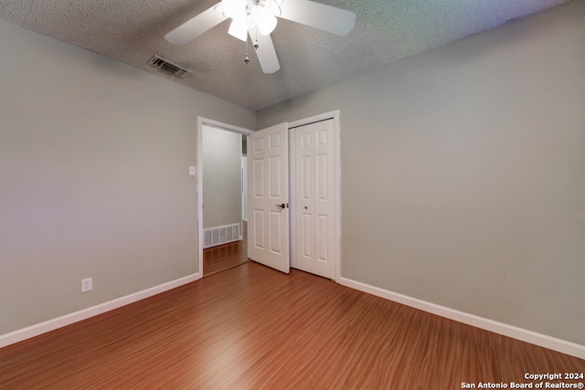 unfurnished bedroom featuring ceiling fan, a closet, a textured ceiling, and hardwood / wood-style flooring