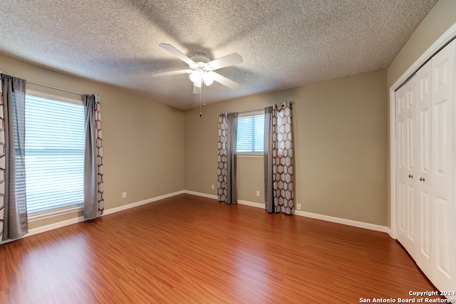 unfurnished bedroom featuring ceiling fan, a closet, a textured ceiling, and hardwood / wood-style flooring