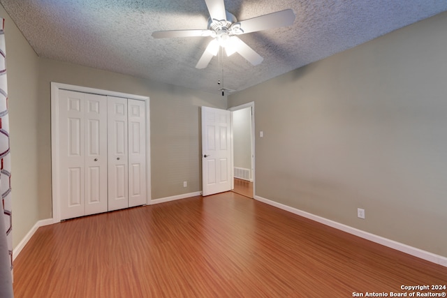 unfurnished bedroom featuring ceiling fan, a closet, wood-type flooring, and a textured ceiling