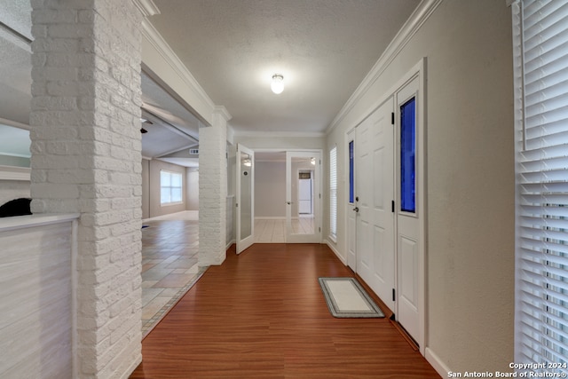 hall with wood-type flooring, a textured ceiling, and ornamental molding