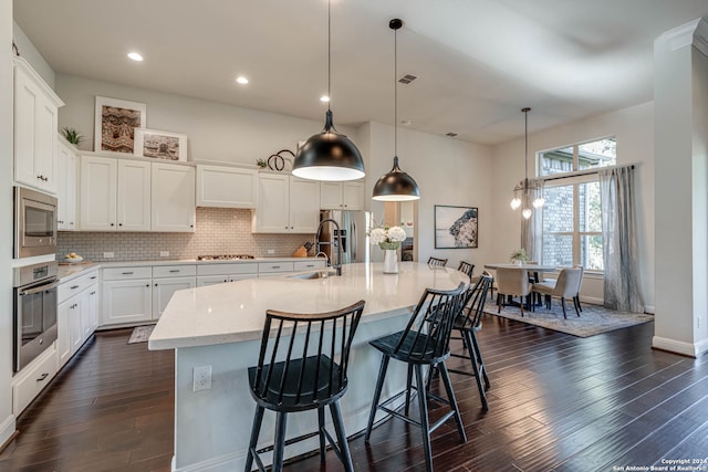 kitchen with hanging light fixtures, an island with sink, appliances with stainless steel finishes, dark hardwood / wood-style flooring, and white cabinetry