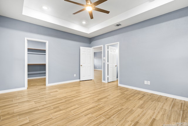 unfurnished bedroom featuring a closet, a walk in closet, a tray ceiling, and ceiling fan