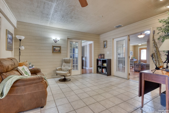 tiled living room featuring french doors, ceiling fan, and wood walls