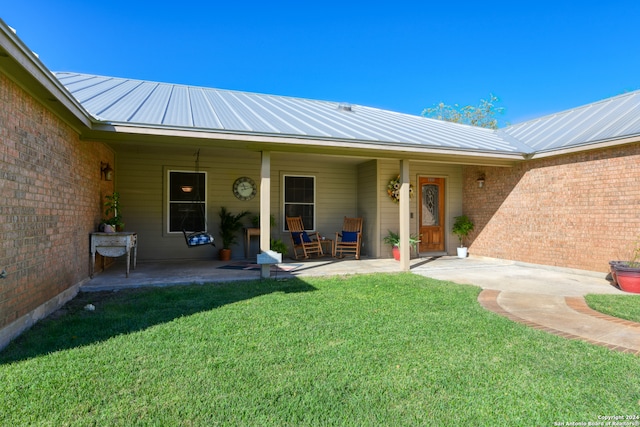 property entrance featuring a patio area, brick siding, metal roof, and a yard