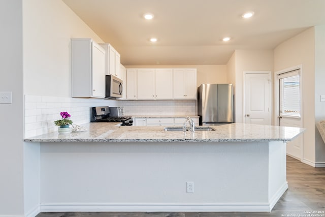 kitchen with kitchen peninsula, appliances with stainless steel finishes, white cabinets, and light stone counters