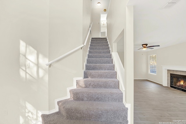 stairs featuring a tile fireplace, ceiling fan, hardwood / wood-style floors, and a towering ceiling