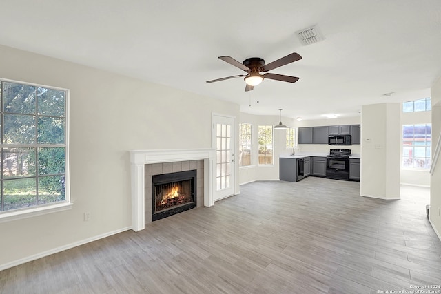 unfurnished living room featuring ceiling fan, light hardwood / wood-style floors, sink, and a tile fireplace