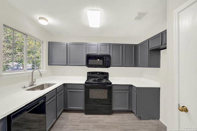 kitchen with black appliances, gray cabinetry, light wood-type flooring, and sink