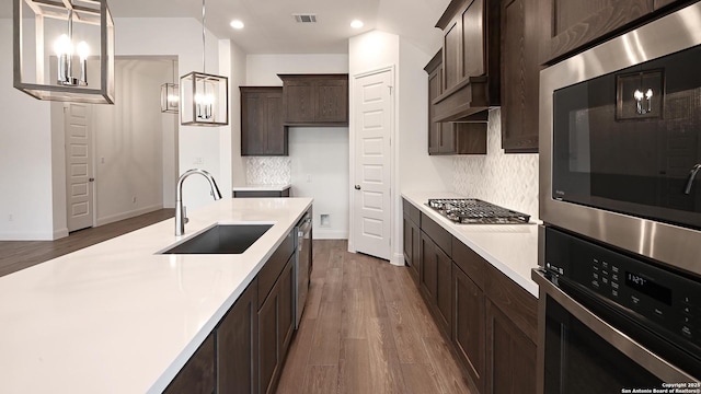 kitchen featuring stainless steel appliances, light countertops, visible vents, a sink, and dark brown cabinetry