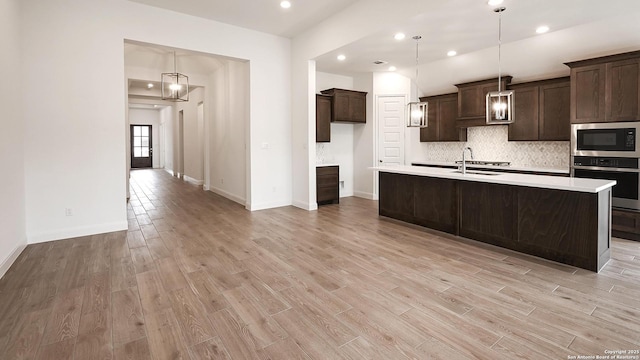 kitchen with decorative backsplash, light wood-style floors, stainless steel oven, dark brown cabinets, and built in microwave