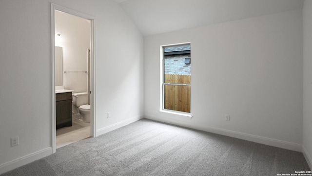 unfurnished bedroom with vaulted ceiling, carpet, ensuite bath, and baseboards