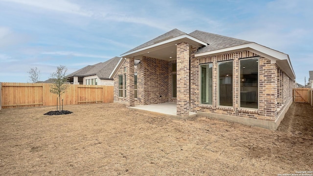 back of property featuring a shingled roof, a patio area, brick siding, and a fenced backyard