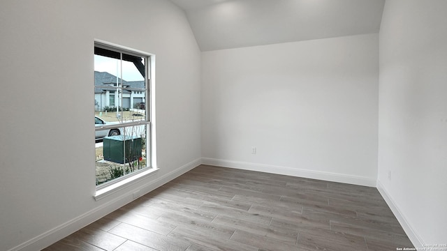 spare room with vaulted ceiling, baseboards, and wood finished floors