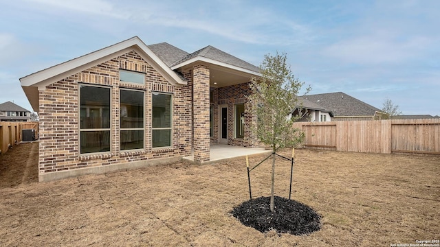 rear view of house with a patio, brick siding, roof with shingles, and a fenced backyard