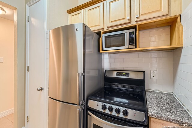 kitchen with tasteful backsplash, light brown cabinetry, stainless steel appliances, and dark stone counters