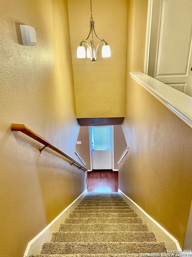 stairs featuring wood-type flooring and an inviting chandelier