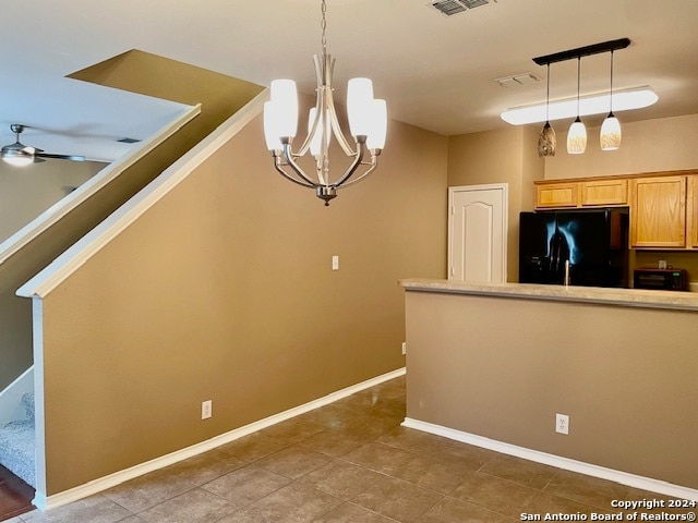 kitchen with dark tile patterned floors, black refrigerator, ceiling fan with notable chandelier, and decorative light fixtures