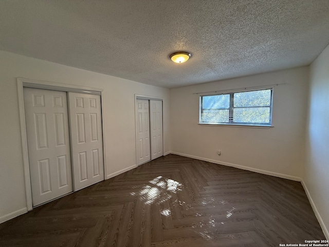 unfurnished bedroom featuring dark parquet flooring, multiple closets, and a textured ceiling