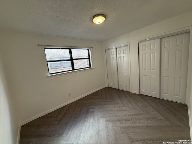 unfurnished bedroom with parquet floors, a textured ceiling, and multiple closets