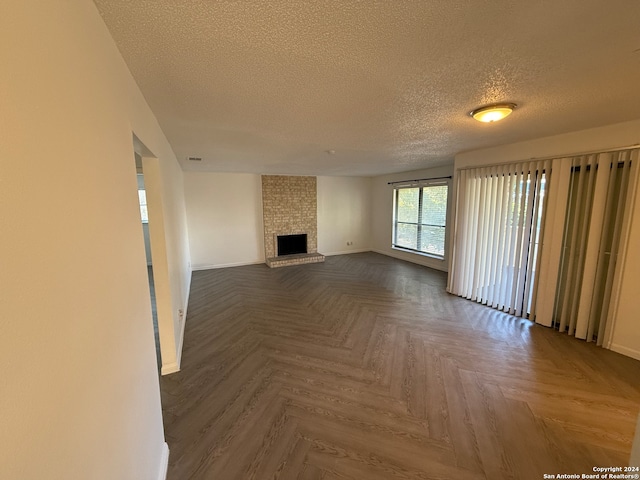 unfurnished living room with a fireplace, a textured ceiling, and parquet flooring