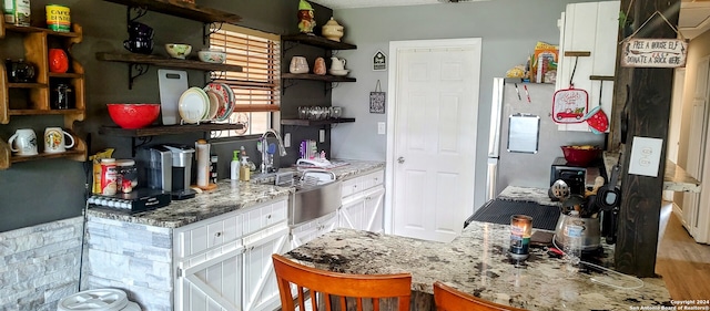 kitchen with a kitchen bar, light wood-type flooring, light stone counters, white refrigerator, and white cabinets