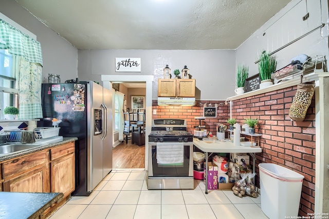 kitchen with sink, light tile patterned floors, stainless steel appliances, and brick wall