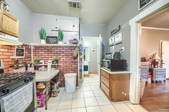 kitchen with appliances with stainless steel finishes, light tile patterned floors, ornamental molding, and exhaust hood