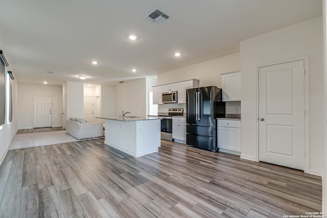 kitchen featuring a center island with sink, light stone countertops, light wood-type flooring, appliances with stainless steel finishes, and white cabinetry