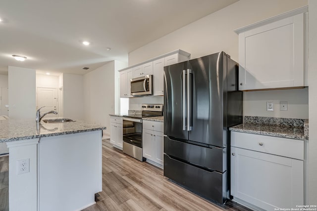 kitchen with appliances with stainless steel finishes, sink, a center island with sink, light hardwood / wood-style flooring, and white cabinetry