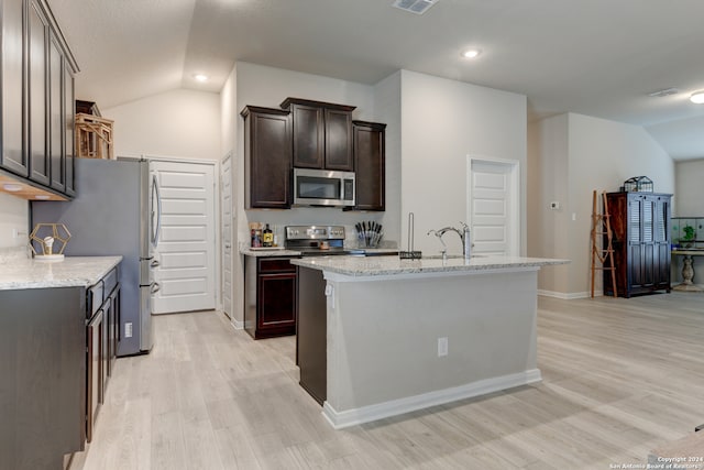 kitchen with stainless steel appliances, light stone counters, light hardwood / wood-style flooring, an island with sink, and vaulted ceiling