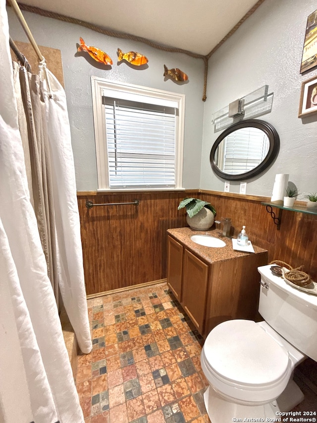 bathroom with vanity, wood walls, toilet, and curtained shower