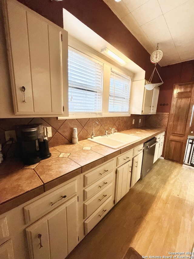 kitchen with decorative backsplash, light wood-type flooring, pendant lighting, tile countertops, and dishwasher