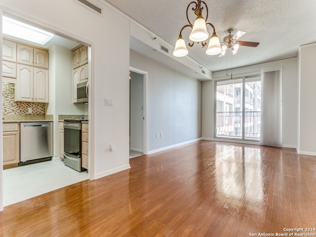 kitchen featuring decorative backsplash, light wood-type flooring, a textured ceiling, stainless steel appliances, and decorative light fixtures