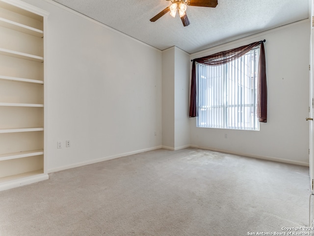 spare room with light carpet, built in features, ceiling fan, and a textured ceiling