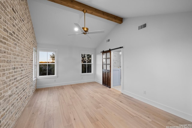 empty room with brick wall, ceiling fan, beam ceiling, a barn door, and light hardwood / wood-style flooring