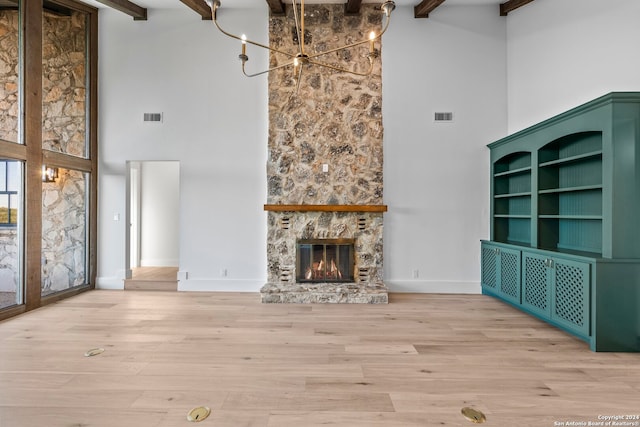 unfurnished living room with an inviting chandelier, light wood-type flooring, a towering ceiling, a fireplace, and beam ceiling