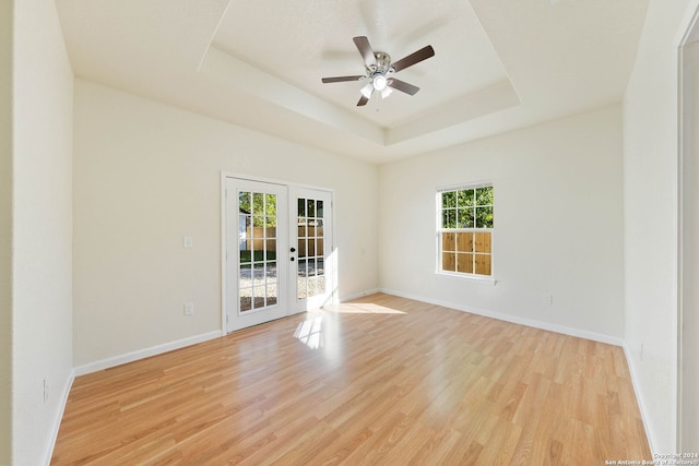 empty room featuring light hardwood / wood-style flooring, a tray ceiling, and french doors