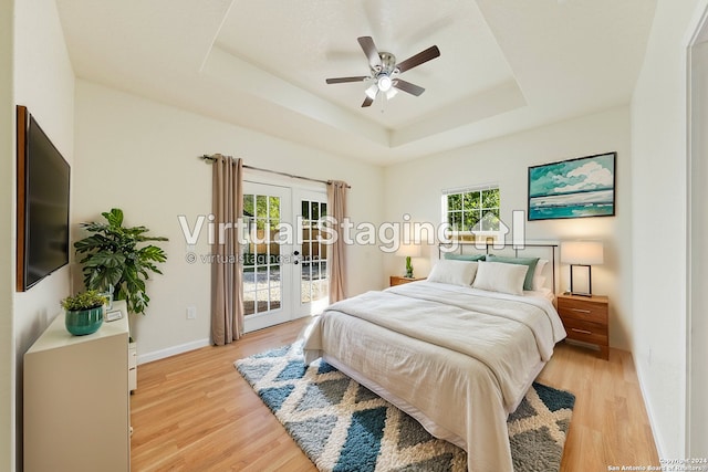 bedroom featuring access to exterior, ceiling fan, french doors, light hardwood / wood-style flooring, and a tray ceiling