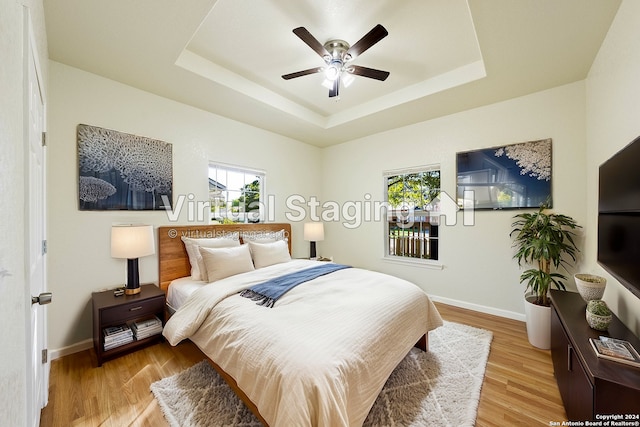 bedroom with a tray ceiling, ceiling fan, and light hardwood / wood-style flooring